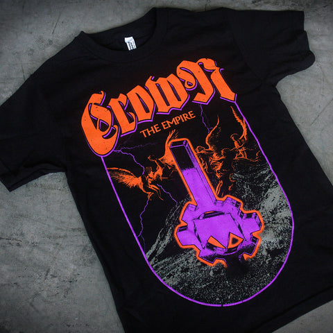 Crown The Empire unisex heavy cotton T-shirt featuring bold orange and purple graphics with winged creatures, lightning, and a gear key design over rocky terrain. Laid flat on a gray surface.