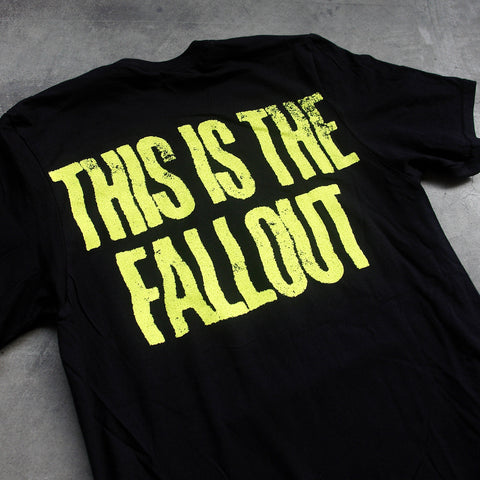 close up, angled image of the back of a black tee shirt laid flat on a concrete floor. tee has yellow text across the shoulders that says this is the fallout.