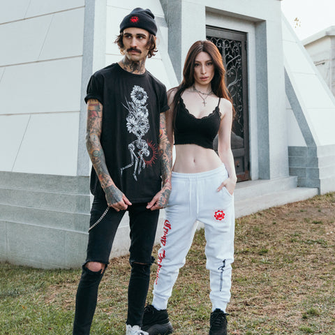 image of white sweatpants worn by a woman standing outside. left leg has red print that says crown the empire. small red print of the crown emblem on the right hip, and black print of a sword on the bottom right leg