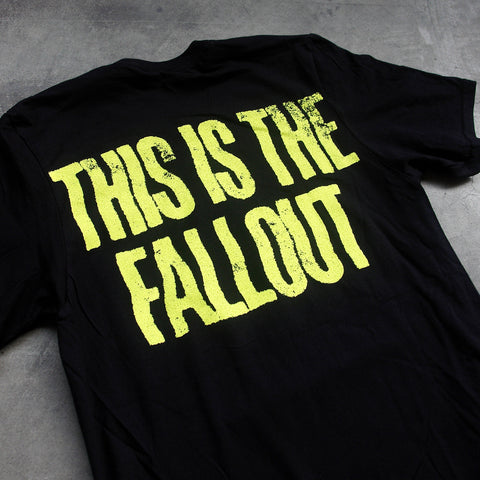 close up, angled image of the back of a black tee shirt laid flat on a concrete floor. tee has yellow text across the shoulders that says this is the fallout.