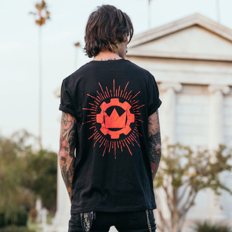 image of the back of a black tee shirt worn by a man with tattoos standing outside. tee has a red print of the crown emblem