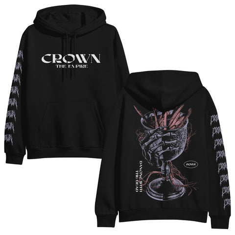 Photo of the front and back of a black hoodie on a white background. The front of the hoodie says crown the empire in white. The sleeves say Crown on them repeatedly in a death metal font in purple. The back of the hoodie features a purple goblet with a skeleton hand wrapped around it. In white are the words dancing with the dead and 2022.